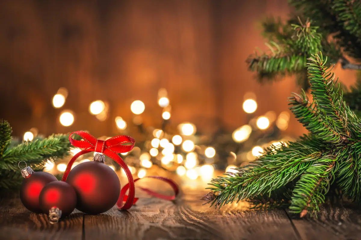 Red Christmas Ornaments on Wood Background and defocused lights. Spruce Tree branch on the left and right.