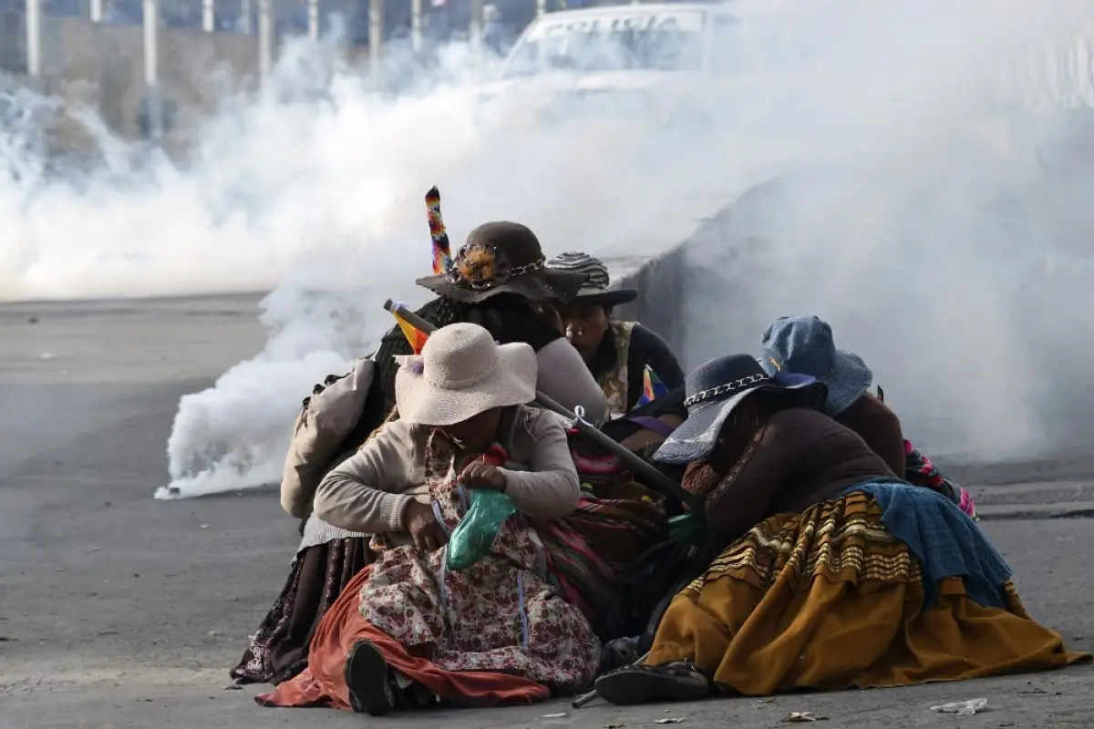 Bolivian indigenous women protect themselves from tear gas during a protest against the interim government in La Paz on November 15, 2019. - Bolivia's interim president Jeanine Anez said Friday that exiled ex-president Evo Morales would have to "answer to