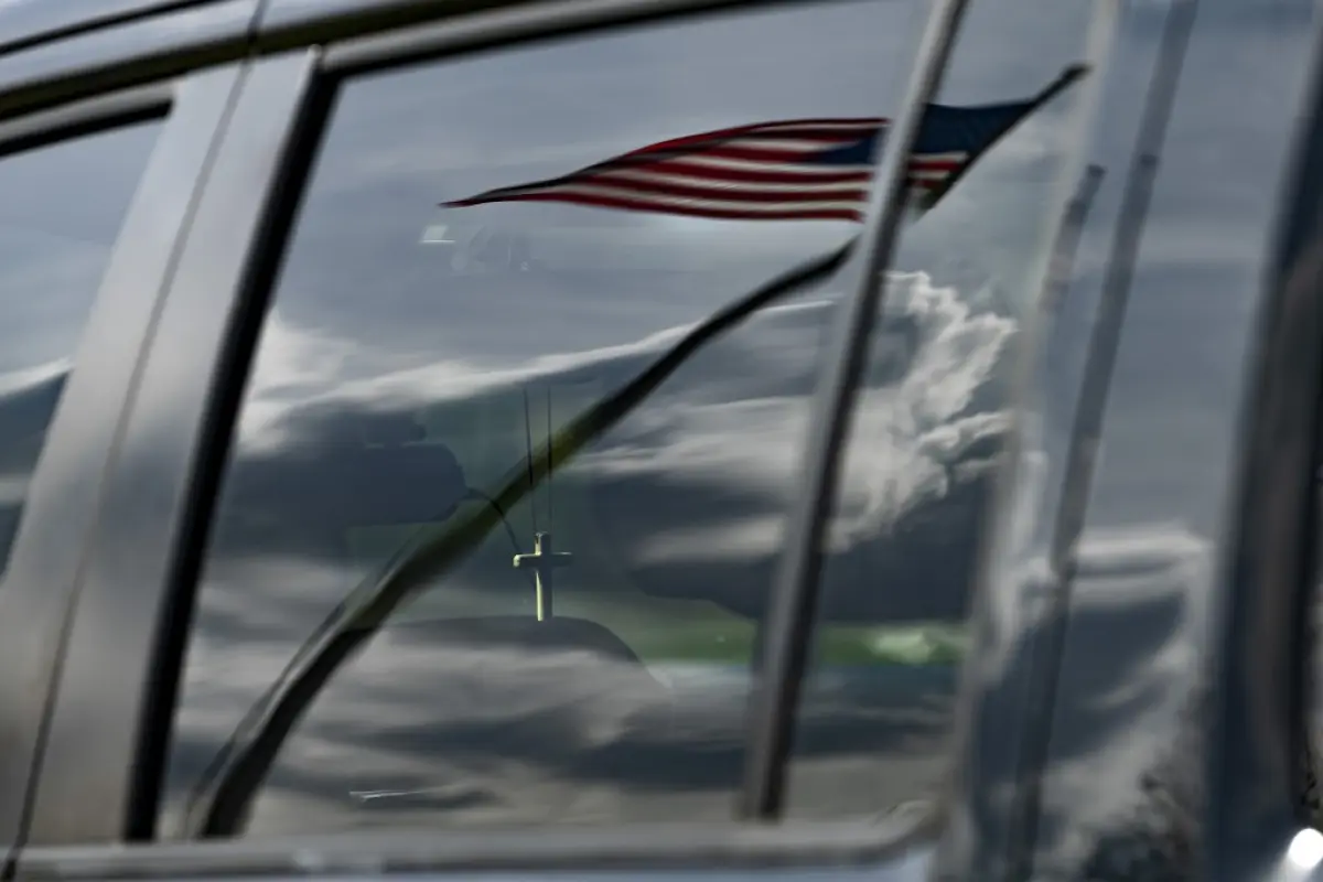 A cross hangs from the rearview mirror of a members car as they listen to Sunday church service held at Great Marsh Park in Cambridge, Maryland, on March 22, 2020. - Pastor Abraham Lankford, who leads Jesus' Church secured the site after concerns over the