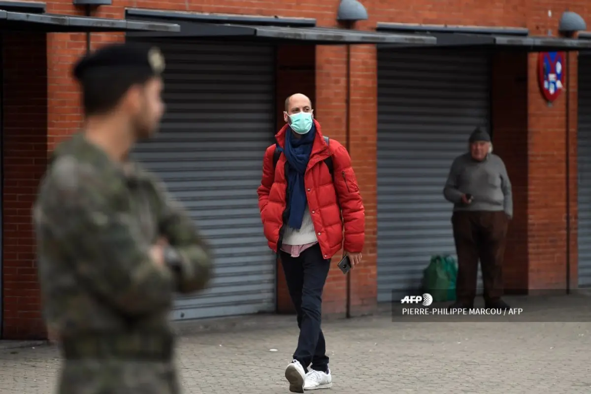 A man wearing a face mask as a protective measure, walks past soldiers deployed at Atocha railway station in Madrid to fight against the spread of the coronavirus COVID-19, on March 18, 2020. - Spanish Prime Minister Pedro Sanchez spoke yesterday with Chi