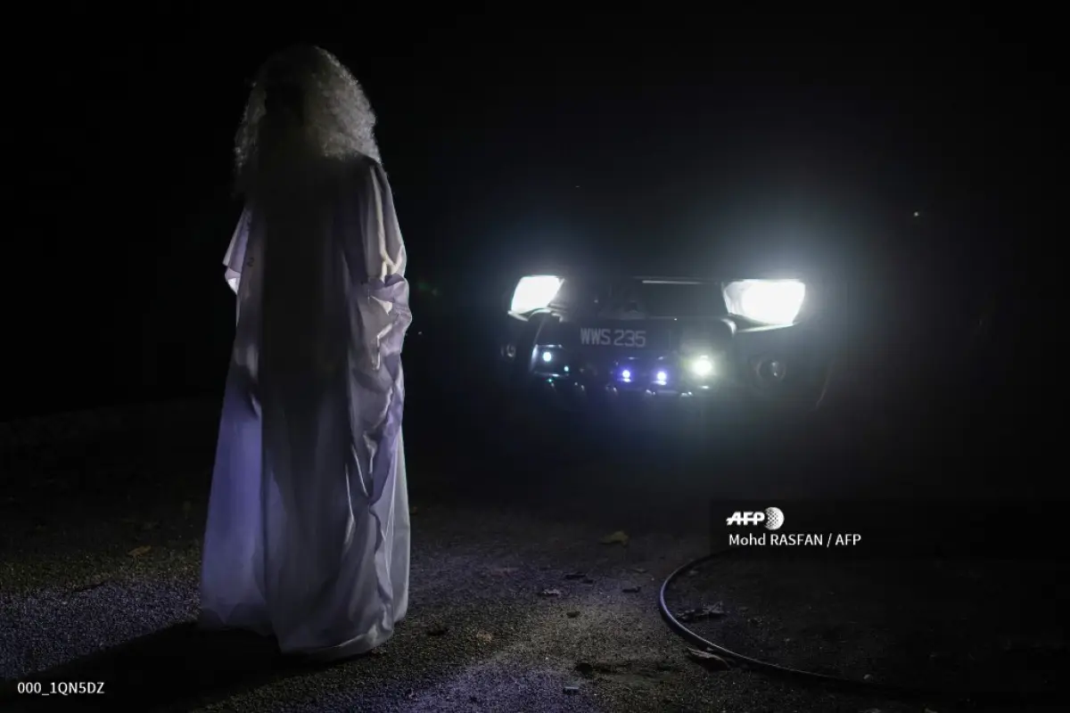 This picture taken on April 16, 2020 shows Urabil Alias, 38, wearing a ghost costume as he stands in front of a car while walking in a residential area to scare people from leaving their houses during the Movement Control Order, limiting the activities of