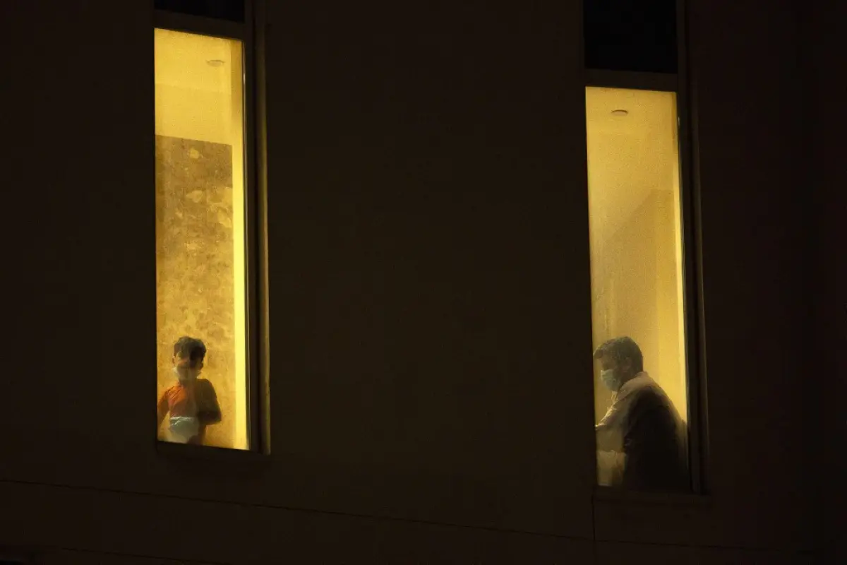 A boy looks through a window as a man wearing a surgical mask sits by at an isolated section for COVID-19 coronavirus disease treatment at a hotel in the sports city of Iraq's southern city of Basra on May 11, 2020. (Photo by Hussein FALEH / AFP)