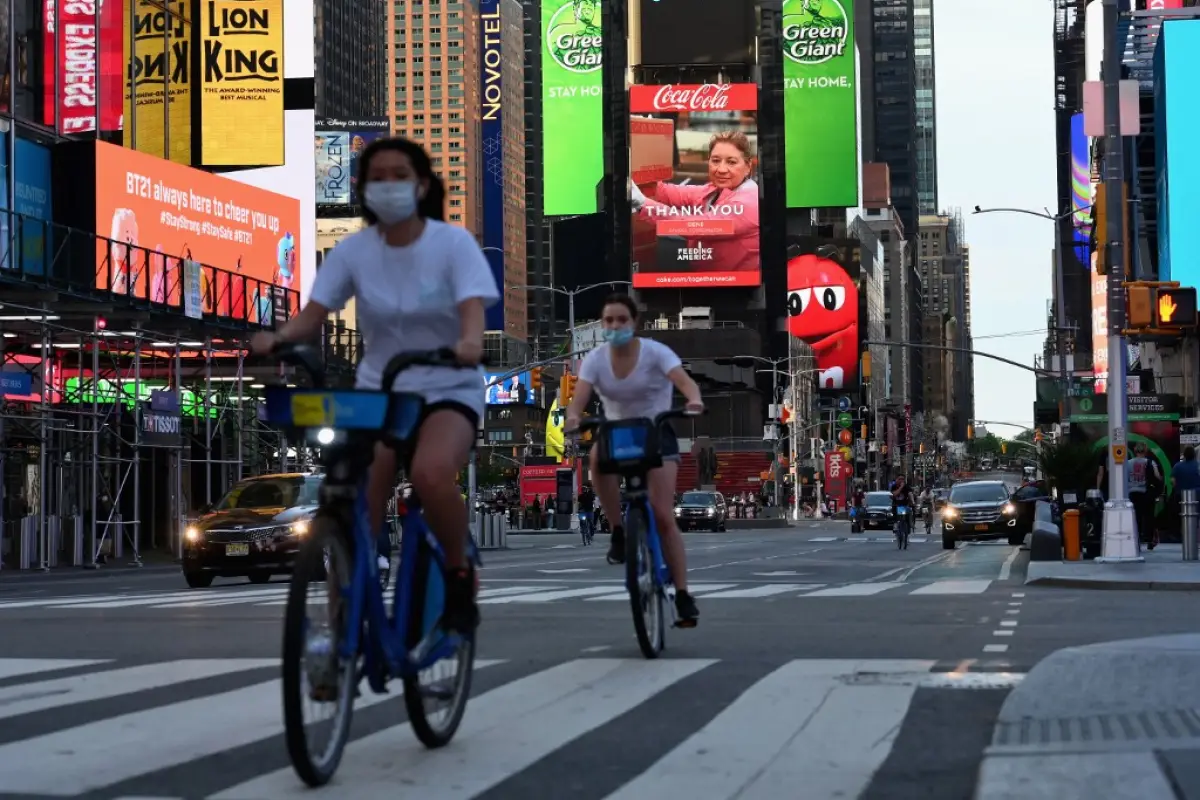 (FILES) In this file photo taken on May 27, 2020 people wearing a facemasks ride their bikes through Times Square in New York City, amid the novel coronavirus pandemic. - New York, the US city worst-hit by the coronavirus, is "on track" to start reopening