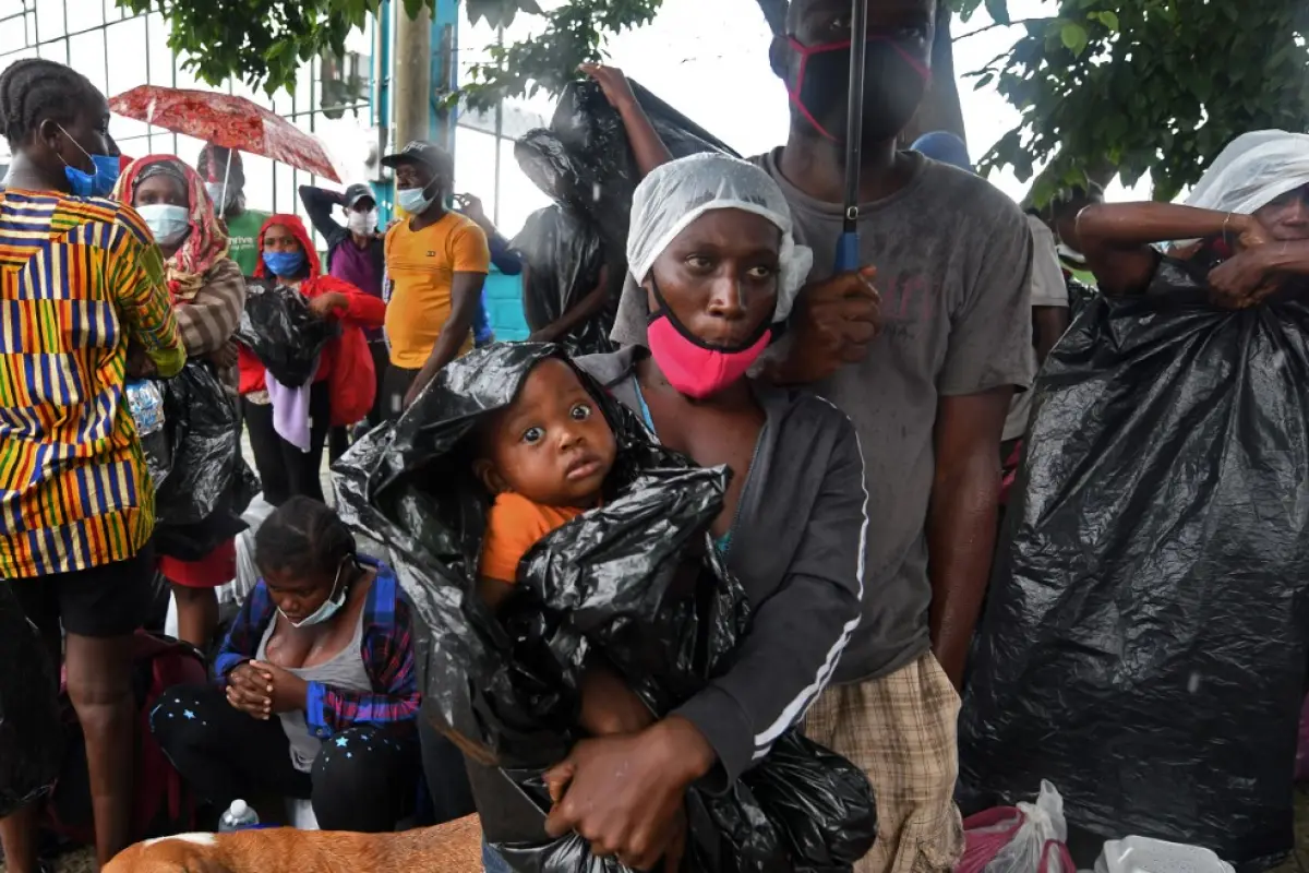 A migrant woman holds a baby wrapped in a plastic bag to protect him from the rain after being stopped while heading in a caravan to the border with Guatemala, at a police station in Cerro de Hula, 10 km south of Tegucigalpa, on June 3, 2020. - Almost a h