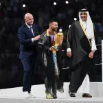 LUSAIL CITY, QATAR - DECEMBER 18: Lionel Messi of Argentina kisses the FIFA World Cup Qatar 2022 Winner's Trophy as Gianni Infantino, President of FIFA, and Sheikh Tamim bin Hamad Al Thani, Emir of Qatar, look on during the FIFA World Cup Qatar 2022 Final