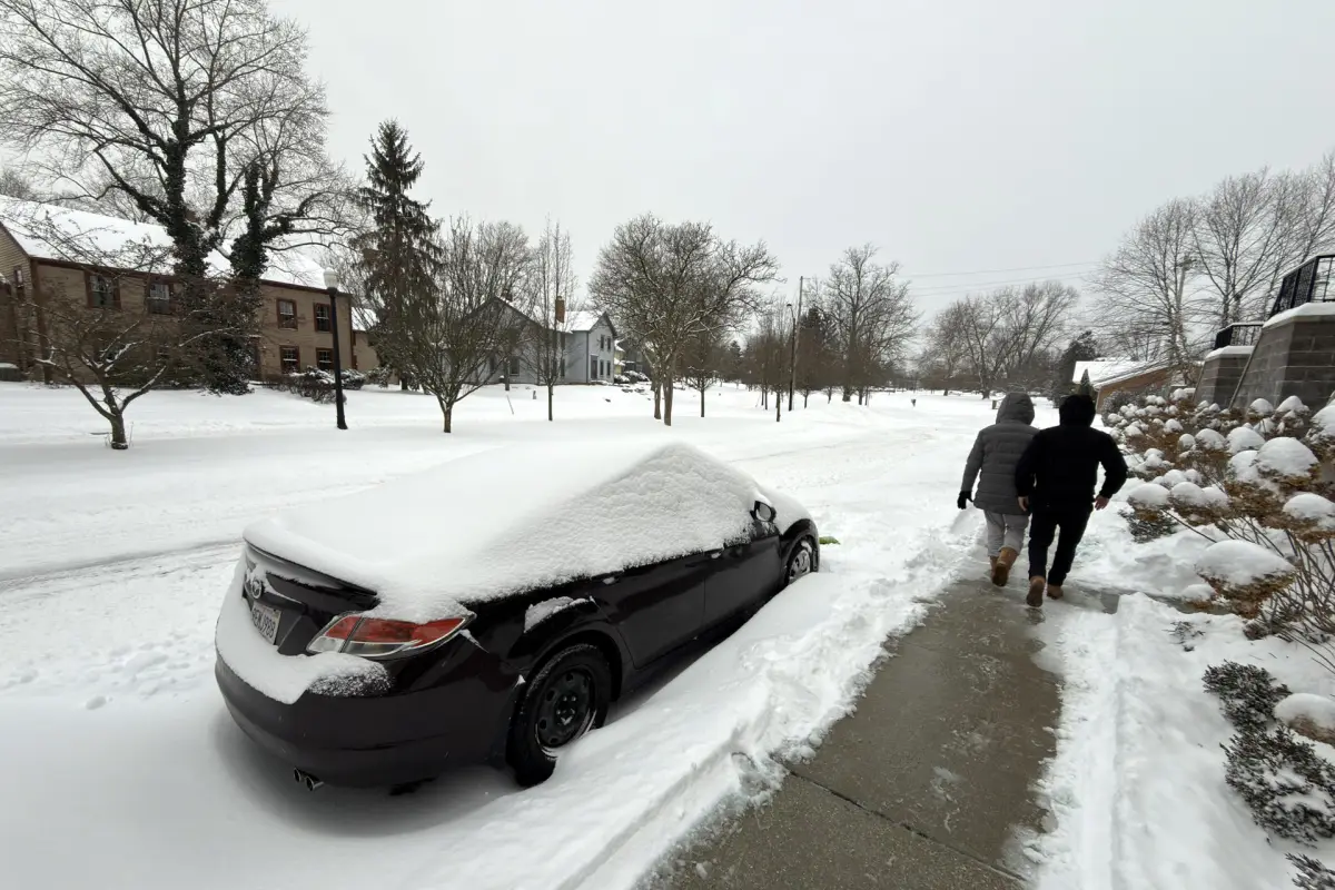 Dos personas caminan al lado de una calle afectada por la nieve este domingo en la ciudad de Hudson, Ohio (EE, UU