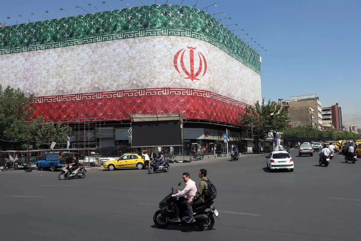 Unos iraníes pasan en coche junto a una valla publicitaria con la bandera nacional de Irán en la plaza Enqelab de Teherán, Irán.,  EFE/Abedin Taherkenareh