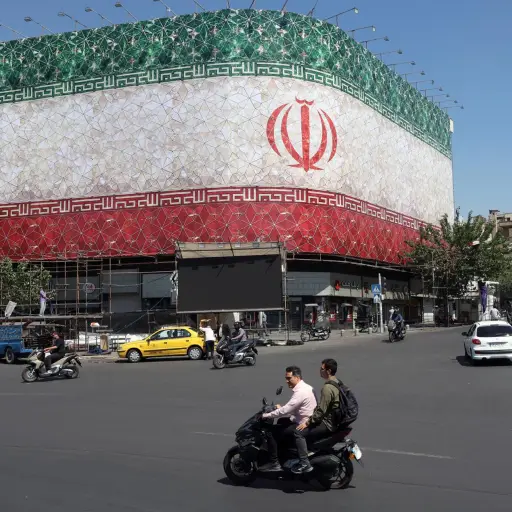 Unos iraníes pasan en coche junto a una valla publicitaria con la bandera nacional de Irán en la plaza Enqelab de Teherán, Irán. , EFE/Abedin Taherkenareh